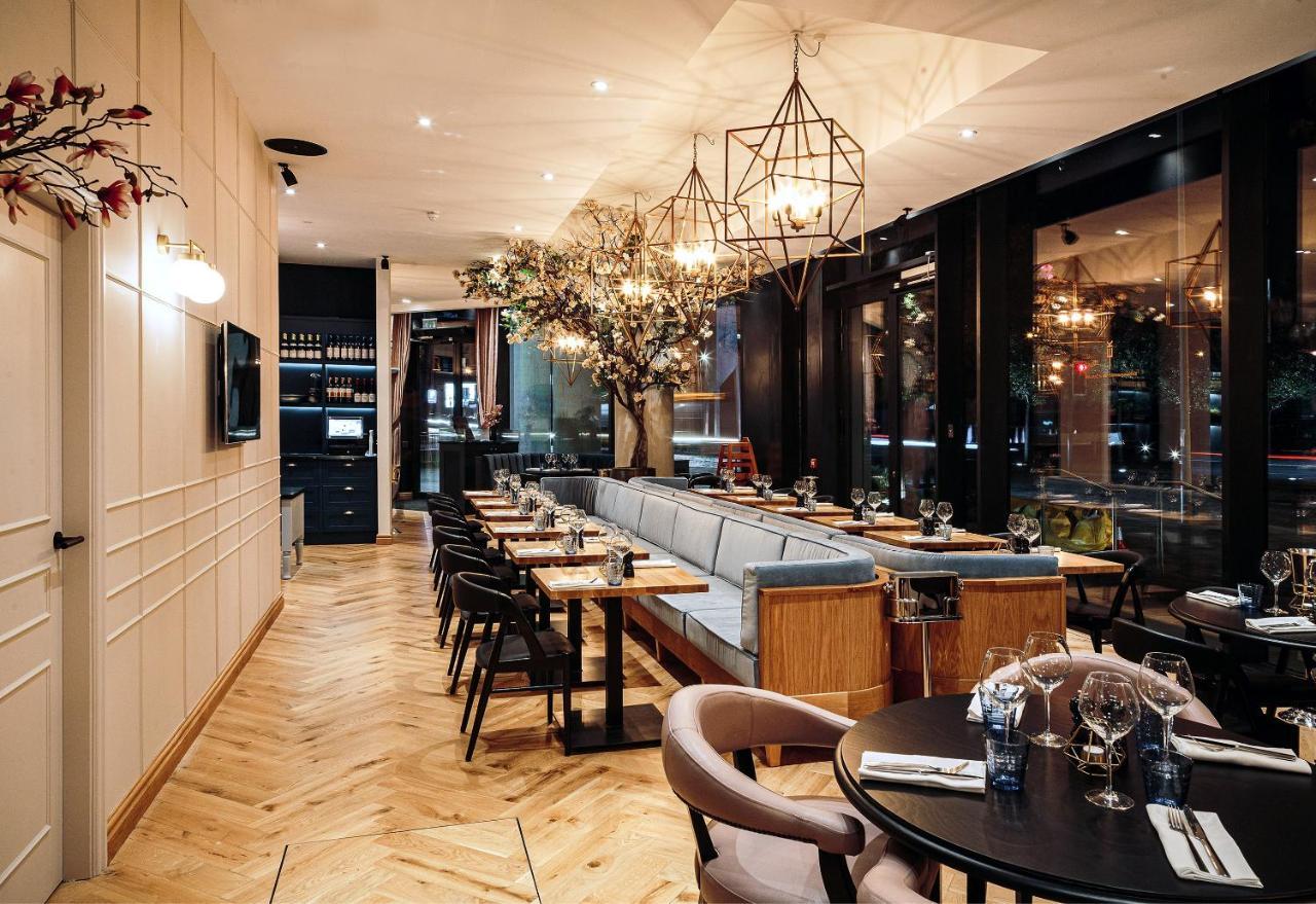 Citysuites Aparthotel Salford  Exterior photo The photo depicts an elegantly designed restaurant interior. The space features a mix of seating options with wooden tables and grey upholstered chairs. There are large windows allowing natural light, and the decor includes stylish pendant lights and