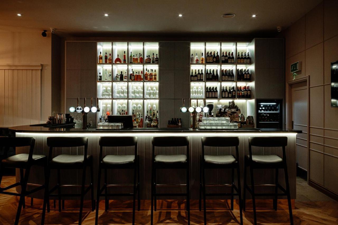 Citysuites Aparthotel Salford  Exterior photo The photo shows a modern bar setup. In the background, there is a well-organized shelf displaying a variety of bottles, illuminated with soft lighting, which creates an inviting atmosphere. The bar counter itself is sleek and minimalistic, with sever