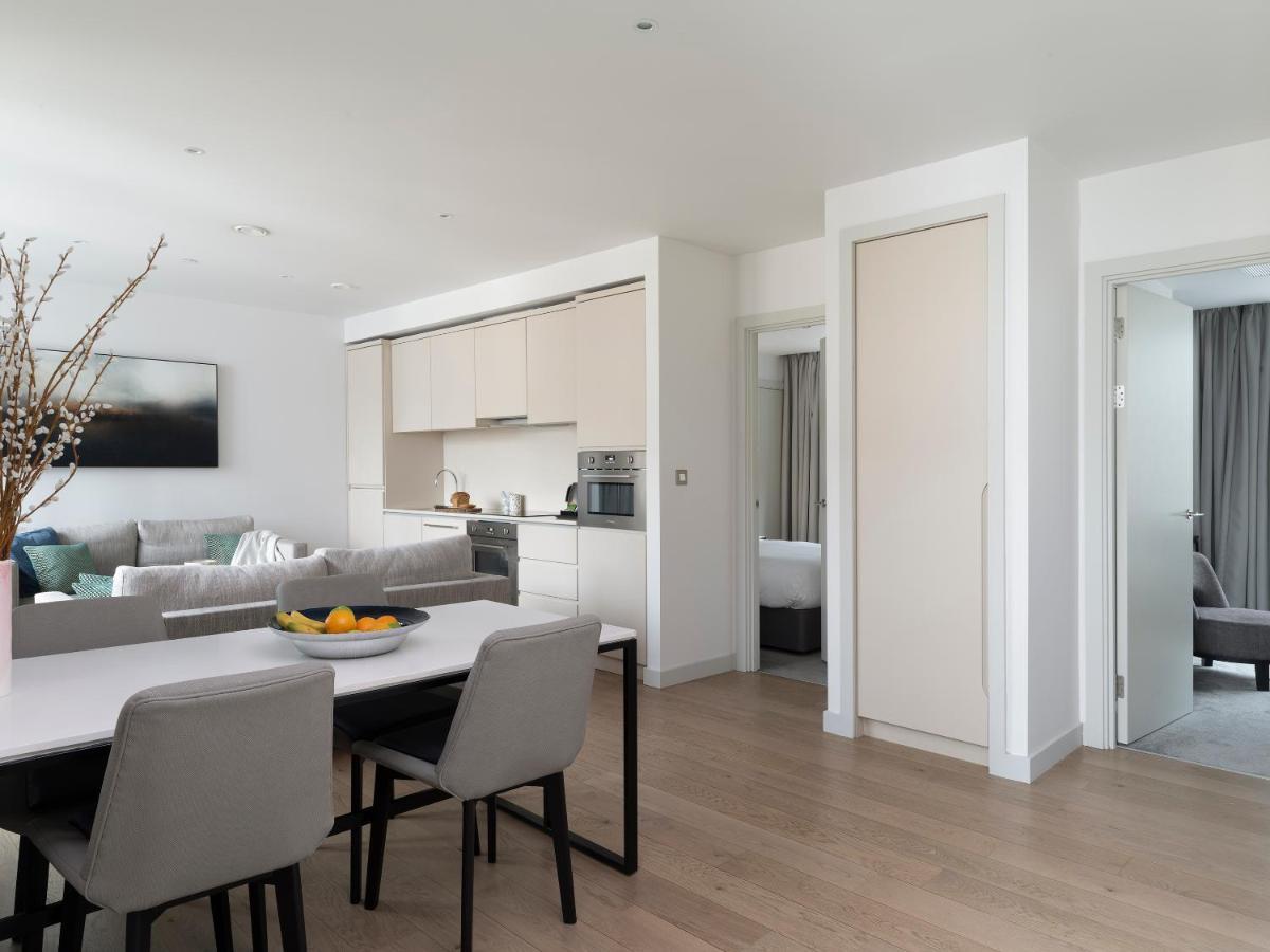 Citysuites Aparthotel Salford  Exterior photo The photo shows a modern, open-concept living space. On the left side, there is a comfortable sitting area with a light-colored sofa, cushions, and a coffee table. In the center of the room, a dining table with several chairs is set up, featuring a f