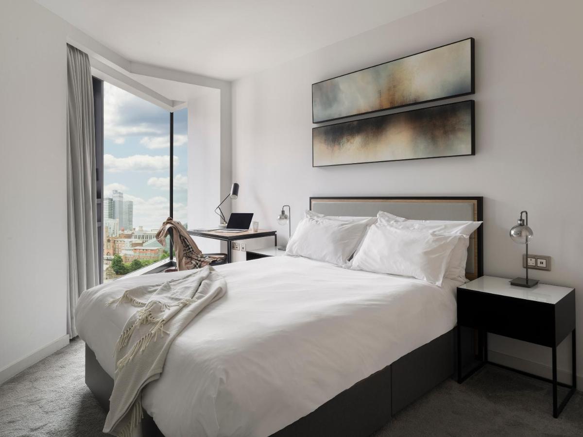 Citysuites Aparthotel Salford  Exterior photo The photo shows a modern bedroom with a minimalistic design. There's a large bed with white bedding, complemented by decorative pillows. To the side of the bed, there are two nightstands, each with a lamp. A stylish piece of art hangs above the bed, 
