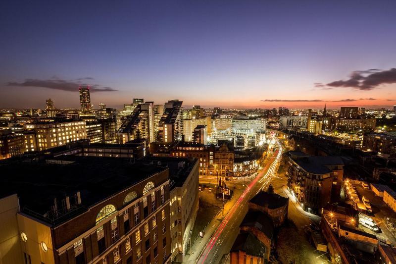 Citysuites Aparthotel Salford  Exterior photo The photo shows a panoramic view of a city during twilight. The skyline is dotted with a variety of modern buildings, showcasing a mix of architectural styles. Streets can be seen winding through the city, illuminated by streetlights and vehicle head