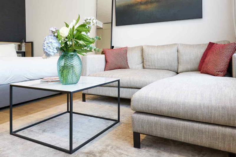 Citysuites Aparthotel Salford  Exterior photo The photo features a modern living area. There is a light-colored, comfortable sectional sofa with decorative cushions in shades of red. A glass coffee table with a black metal frame is positioned in front of the sofa. On the table, there is a striki
