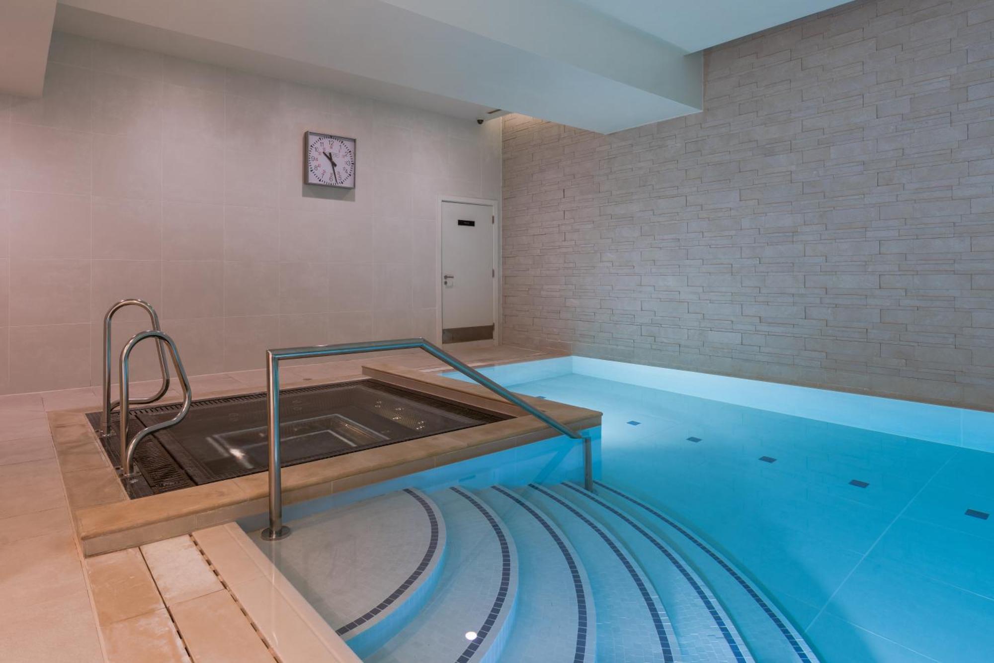 Citysuites Aparthotel Salford  Exterior photo The photo shows a modern spa area featuring a small indoor pool and a hot tub. The pool is designed with a light blue color, and there are steps leading down into it. Next to the pool, there is a hot tub with a stainless steel railing for access. The
