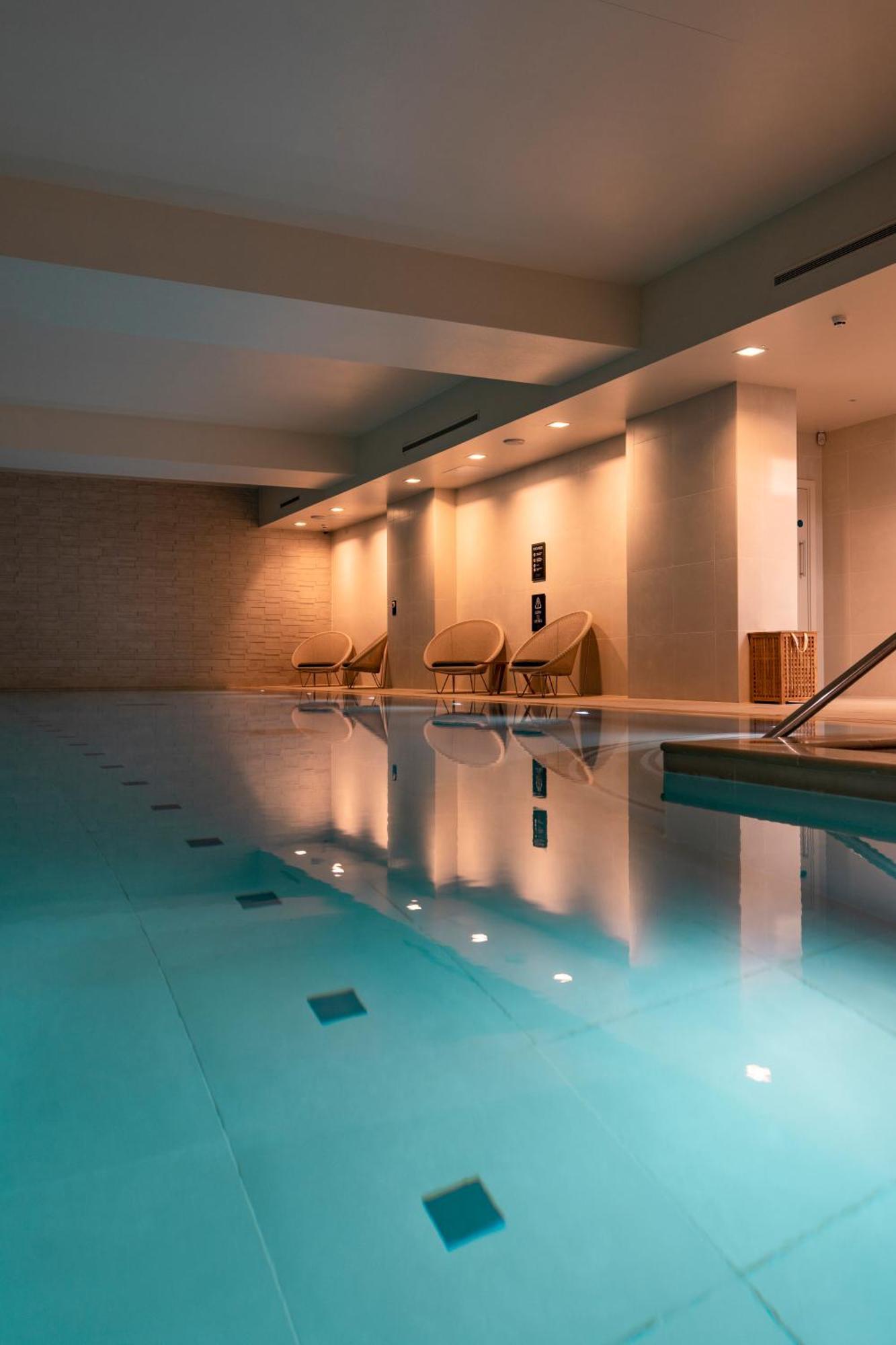 Citysuites Aparthotel Salford  Exterior photo The photo depicts an indoor swimming pool area. The water is clear and blue, reflecting the soft lighting above. There are several lounge chairs arranged near the pool, providing a relaxing space. The walls are painted in neutral tones, contributing 