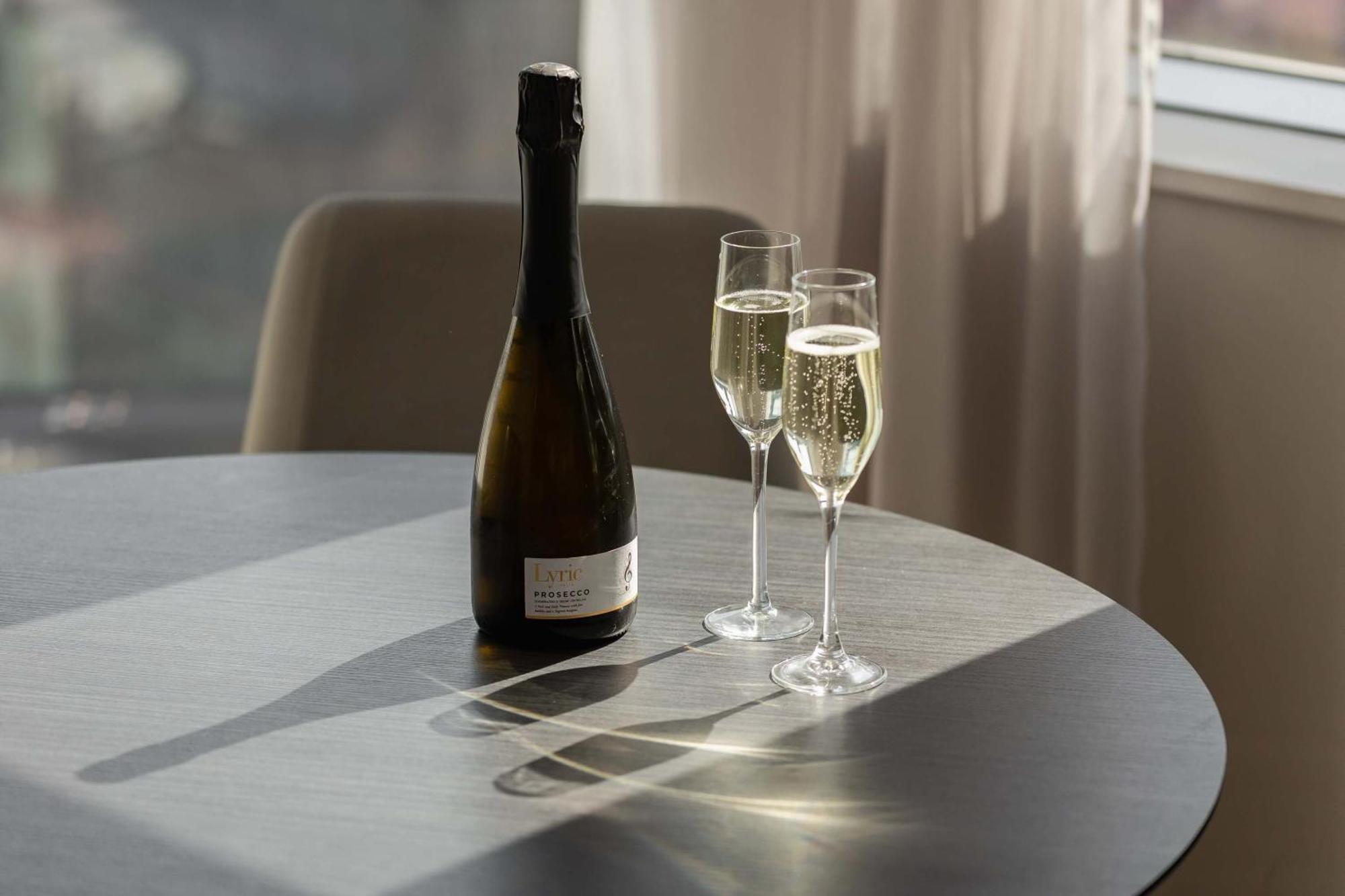 Citysuites Aparthotel Salford  Exterior photo The photo shows a bottle of sparkling wine sitting on a round table alongside two filled champagne flutes. The flutes are positioned upright, with light reflecting off the bubbles in the wine. The setting has a warm atmosphere, enhanced by natural li