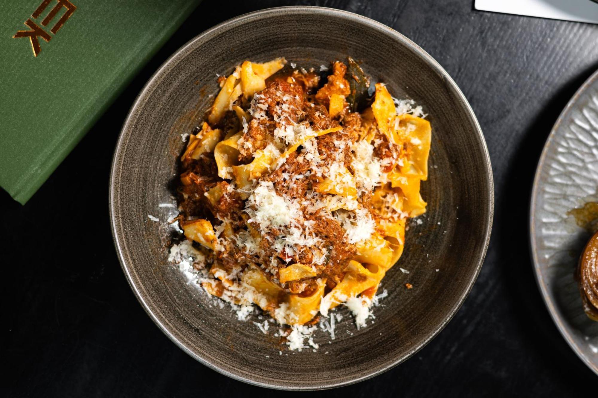 Citysuites Aparthotel Salford  Exterior photo The photo features a bowl of pasta, likely pappardelle, topped with a rich meat sauce. The dish is garnished with a generous amount of grated cheese, adding a creamy texture to the meal. It's presented in a dark, round bowl, which highlights the vibr