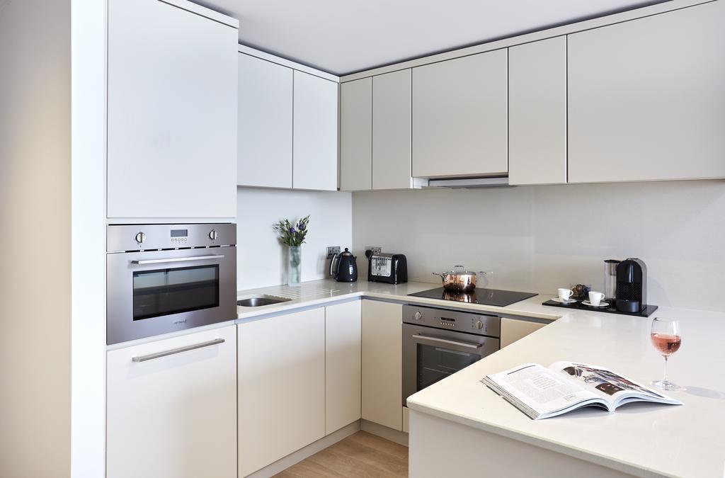 Citysuites Aparthotel Salford  Exterior photo The photo shows a modern kitchen with a sleek and minimalist design. The cabinetry is predominantly white, with smooth, flat surfaces. 

There is an oven built into the cabinetry, along with a stovetop. On the countertop, you can see a coffee maker, 