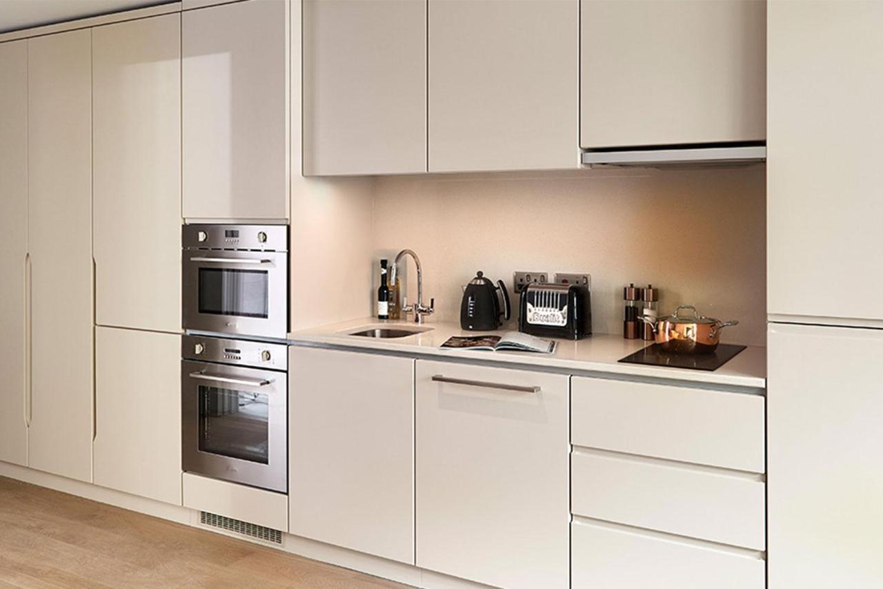 Citysuites Aparthotel Salford  Exterior photo The photo shows a modern kitchen with a sleek and minimalist design. The cabinetry is light-colored, likely a beige or white, giving the space a bright and open feel. 

1. **Oven and Microwave**: There are built-in kitchen appliances, including an ov
