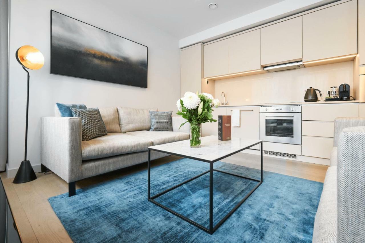 Citysuites Aparthotel Salford  Exterior photo The photo shows a modern living space with a cozy and contemporary design. There is a light grey sofa with plush cushions, positioned in front of a sleek coffee table with a black metal frame. On the table, there is a vase with fresh flowers, adding 